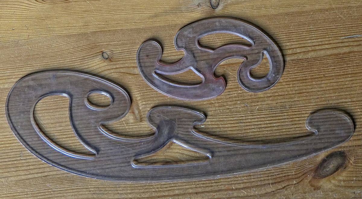 Zwei durchsichtige Kurvenlineale aus Kunststoff auf einem Holztisch